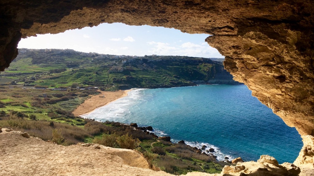 Ramla Bay framed by Tal-Mixta Cave: red sand, turquoise water, terraced hills, Gozo, Malta.